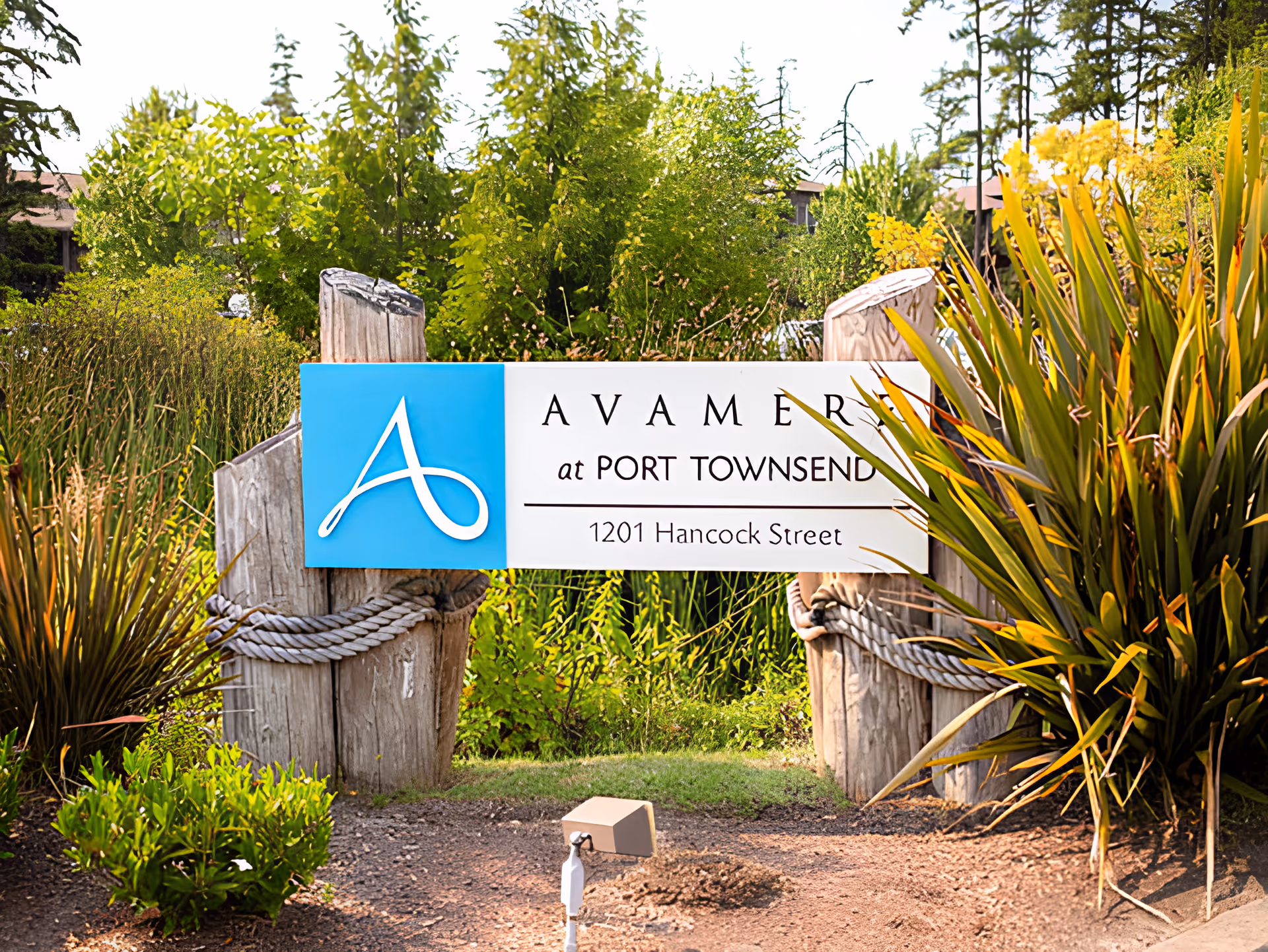 Entrance sign reading "Avamere at Port Townsend 1201 Hancock Street" mounted on wooden posts among landscaped plants.