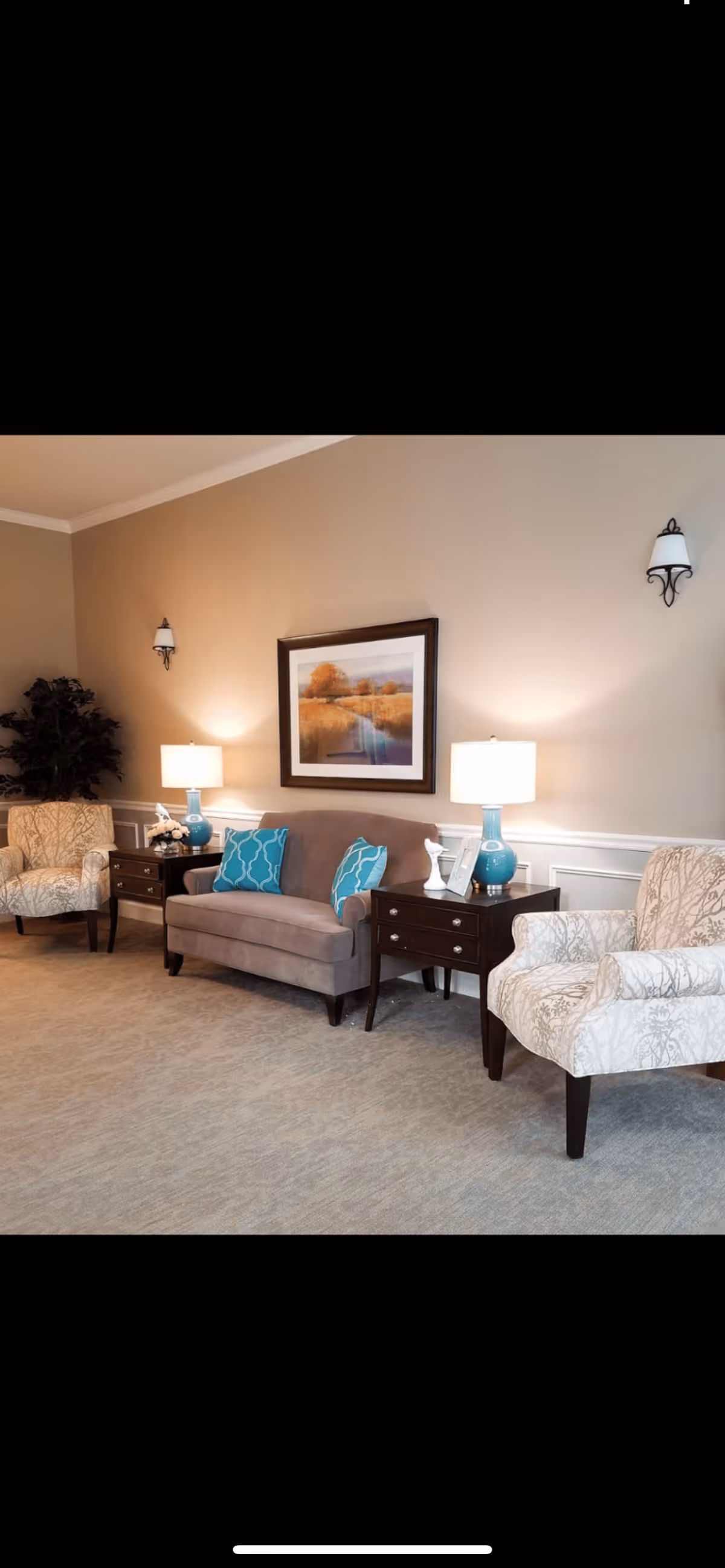 A cozy sitting area with a loveseat, two armchairs, side tables with lamps, and framed wall art in a neutral-toned room.