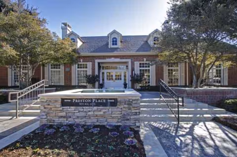 Front entrance of Preston Place senior living facility with stairs, railing, and landscaping.
