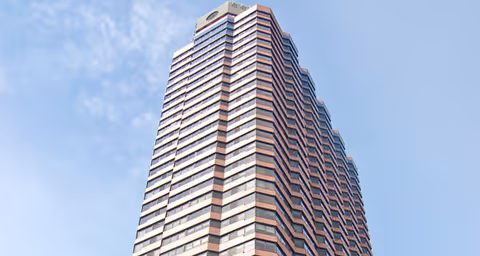 Tall multi-story building with a modern design under a partly cloudy blue sky.