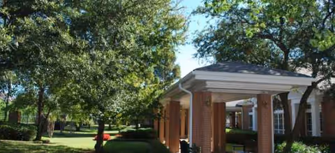 Brick facility entrance with a covered porch, surrounded by trees and manicured lawn.