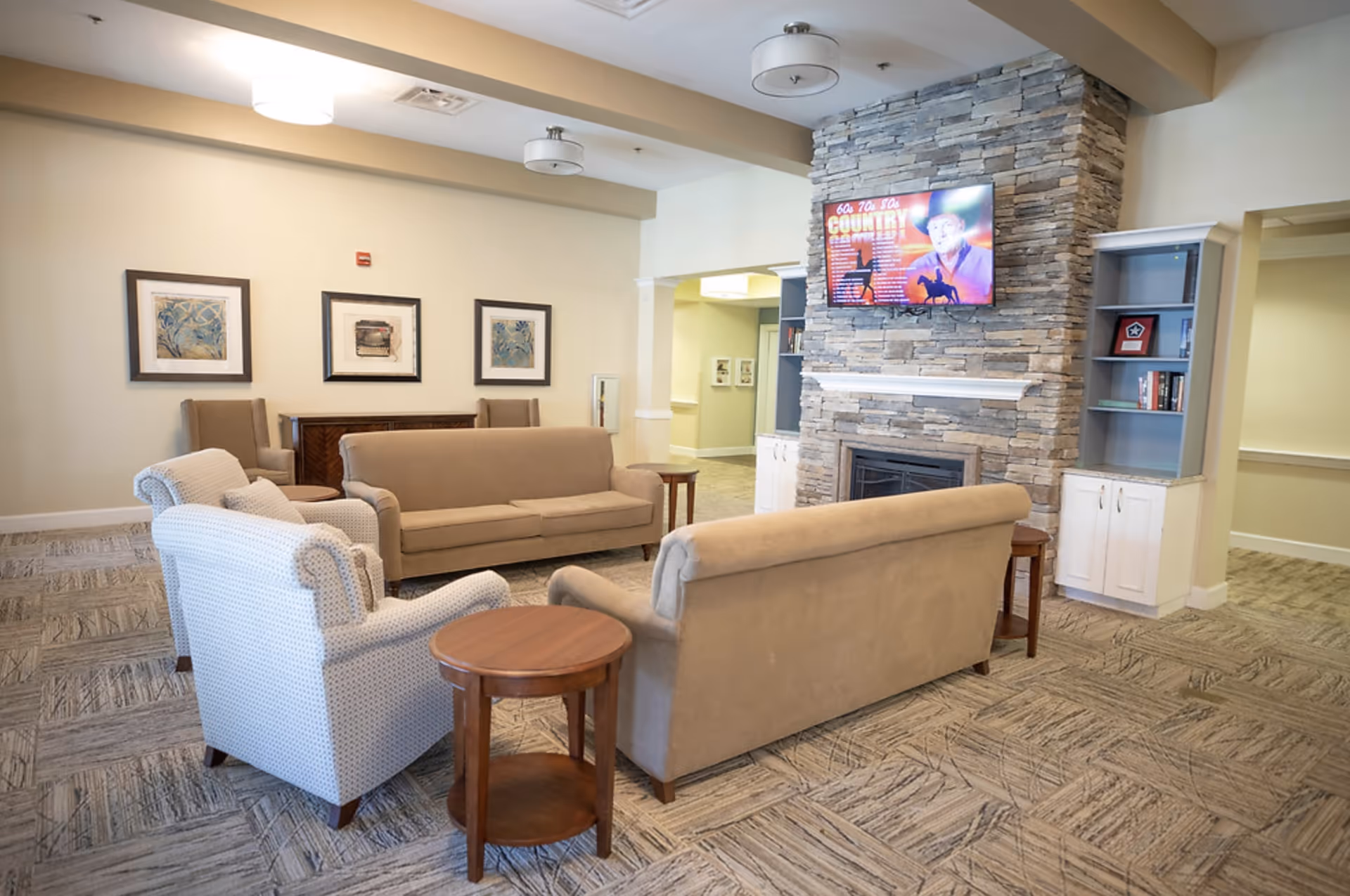 Common area lounge with sofas and armchairs arranged around a stone fireplace and wall-mounted TV.