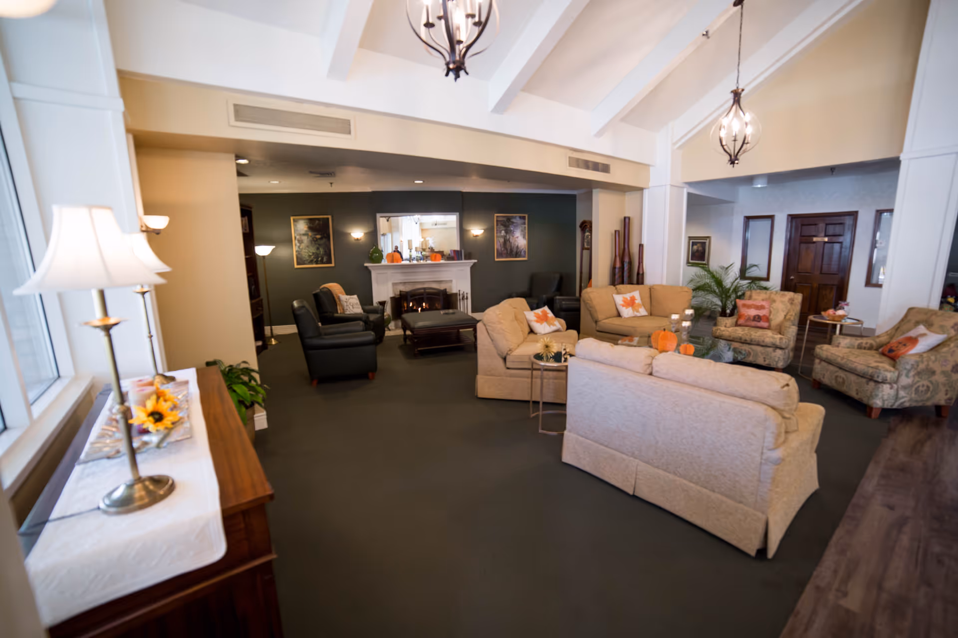 Cozy communal living room in a retirement community with sofas, armchairs, lamps, and a fireplace.