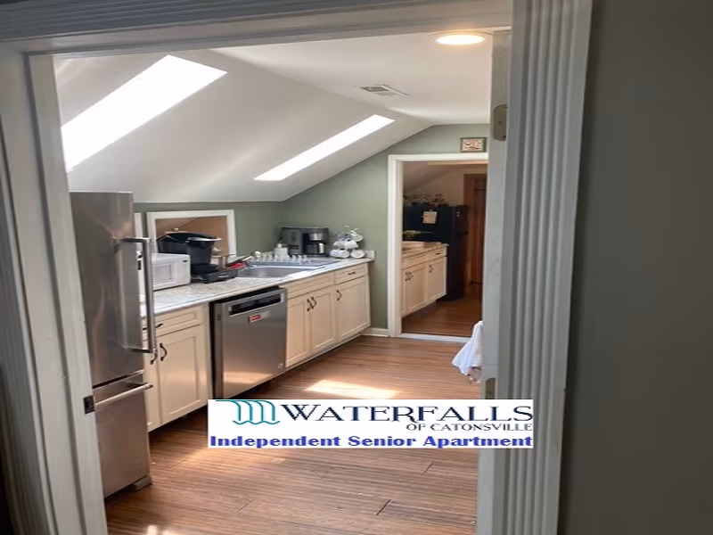 Galley-style kitchen with skylights, white cabinets, stainless steel refrigerator and dishwasher, and wood flooring.