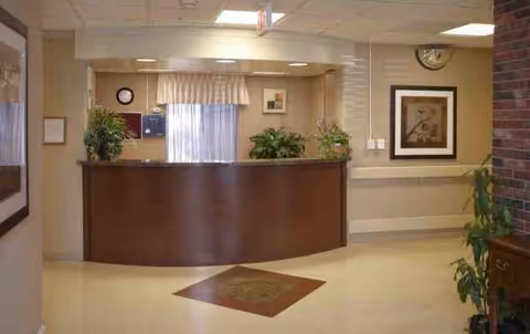 Reception desk in a warmly lit lobby with plants, windows, and framed art.