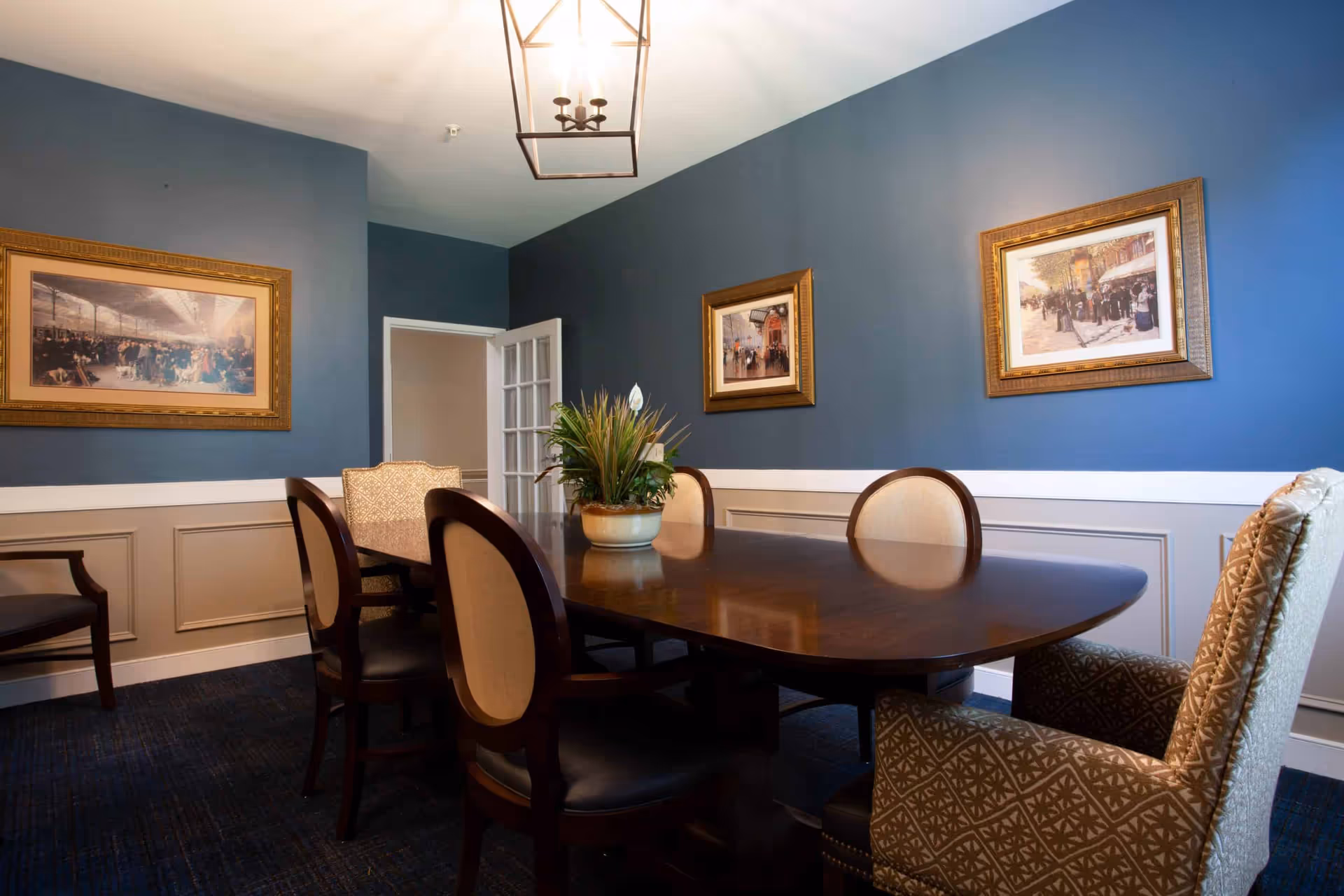 Formal dining room with a dark wood table, upholstered chairs, blue walls, and framed artwork.