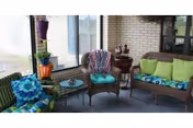 Screened porch with wicker chairs and loveseat arranged around a small table, decorated with colorful cushions and potted plants.