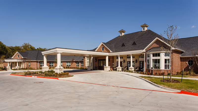 Single-story brick senior living building with a covered porte-cochère entrance and clear blue sky