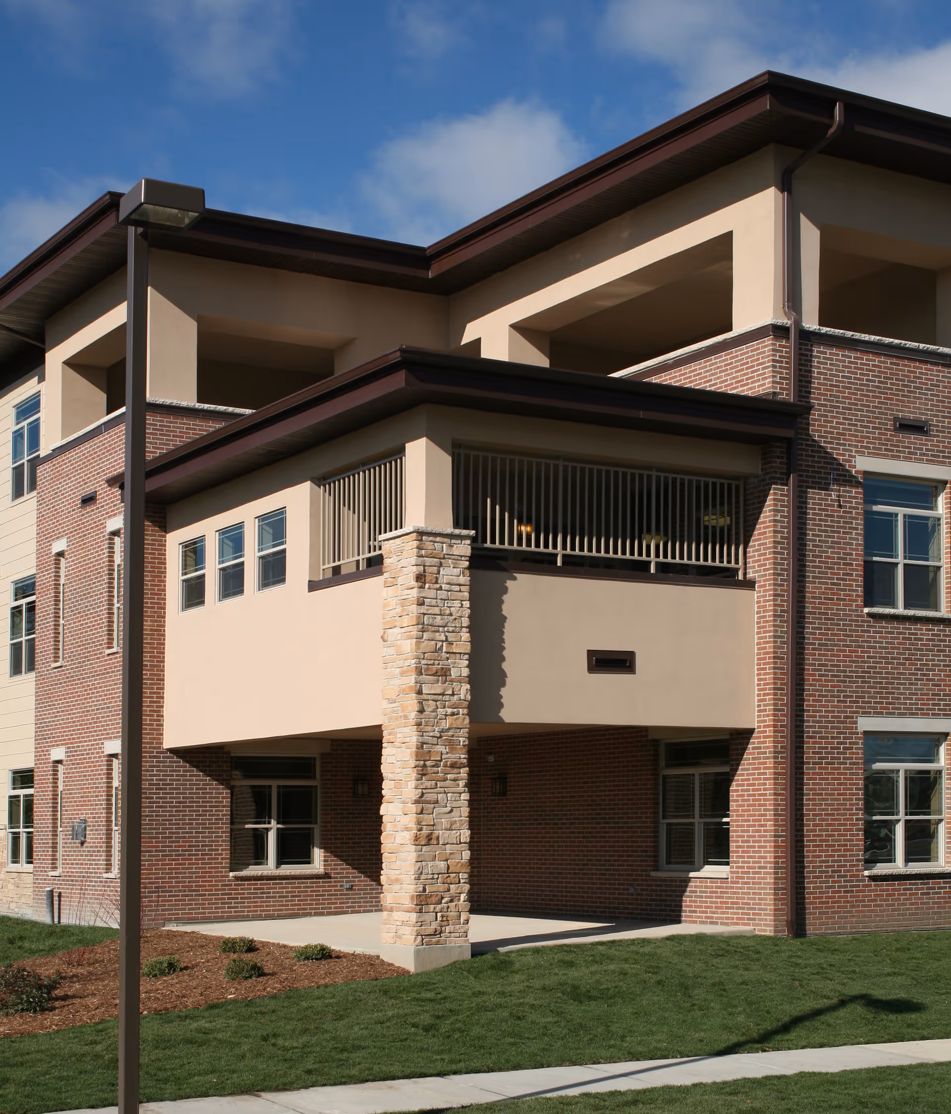 Front exterior of a multi-story brick and stucco building with balconies, a stone column, and a small lawn.