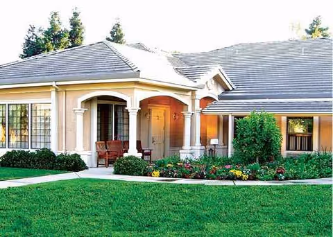 Front view of a memory care facility with arches, entrance, and manicured lawn.