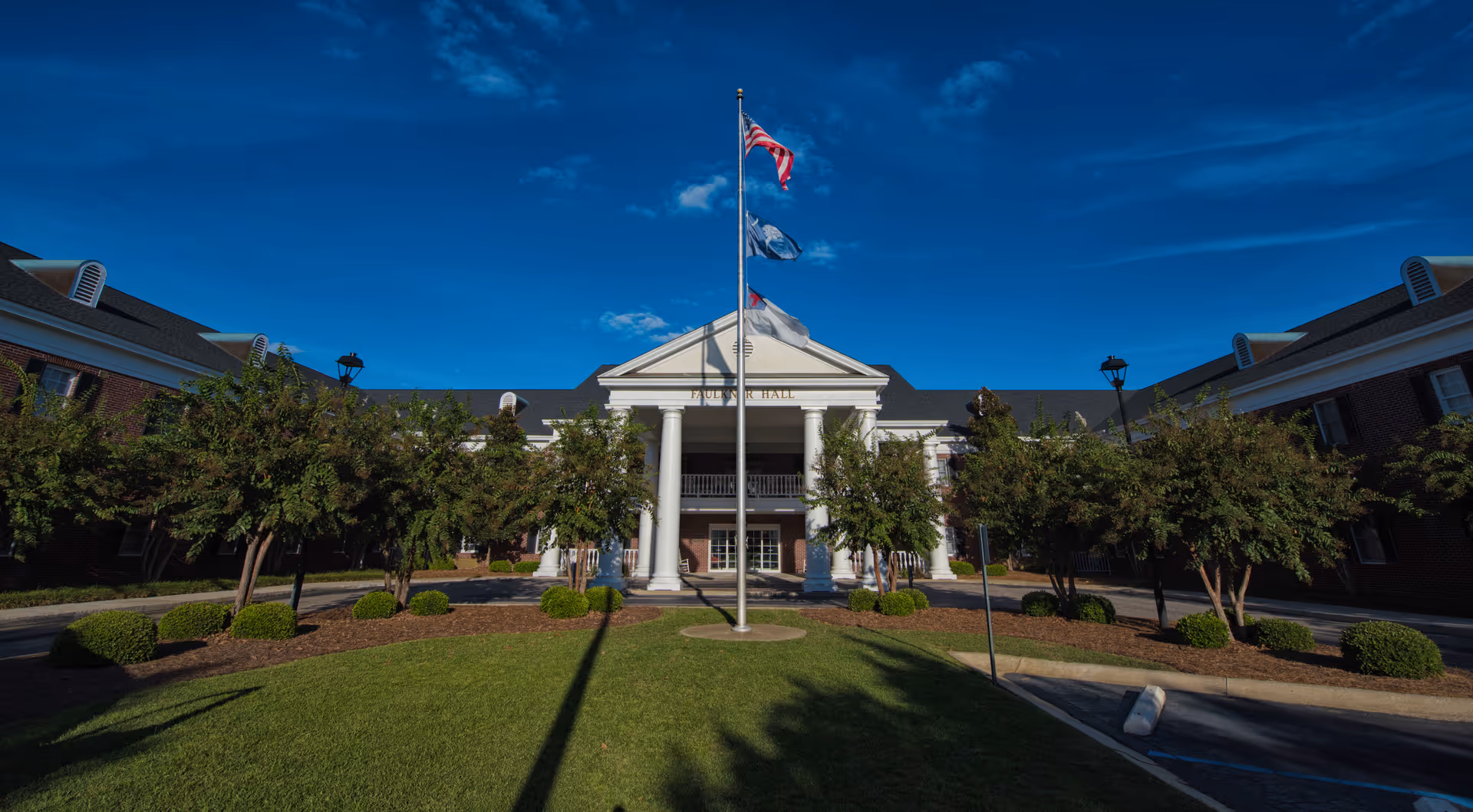 Front view of a senior living facility entrance with columns, flagpole, and landscaping
