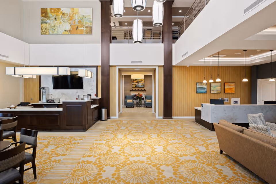 Two-story senior living lobby with reception desks, seating areas, and hanging pendant lights.