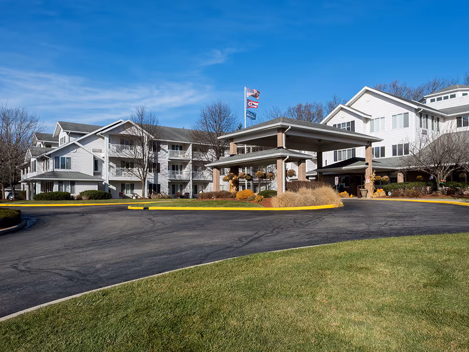 Exterior view of Holiday Alexis Gardens senior living facility with entrance canopy and flags.
