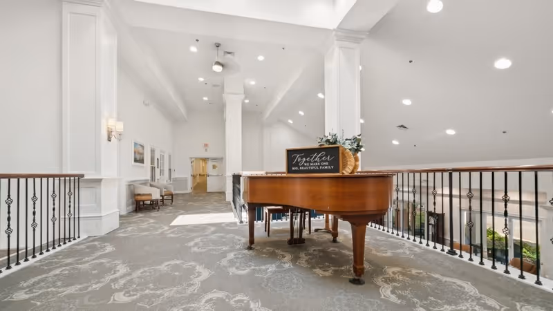 Bright, elegant interior mezzanine with a grand piano on patterned carpet overlooking an open atrium.