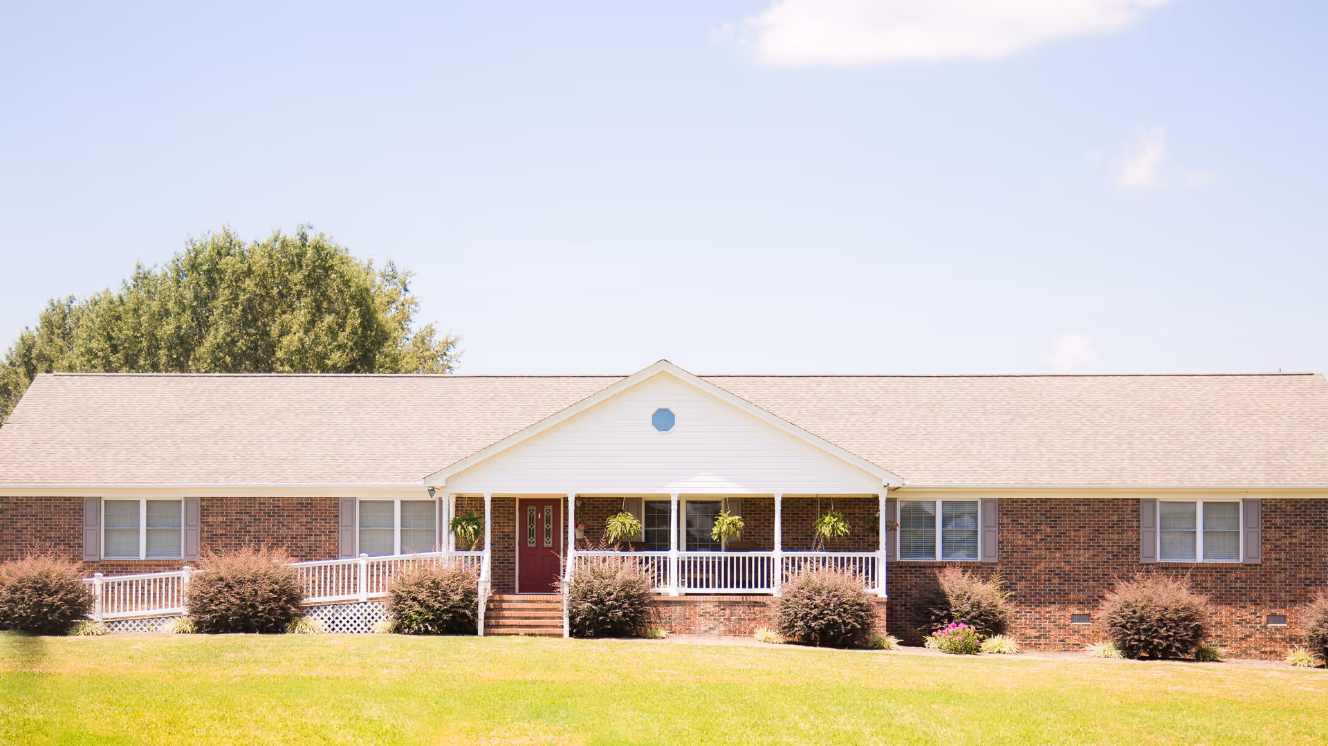 Single-story brick building with a central covered porch, ramp and front lawn under a clear sky.