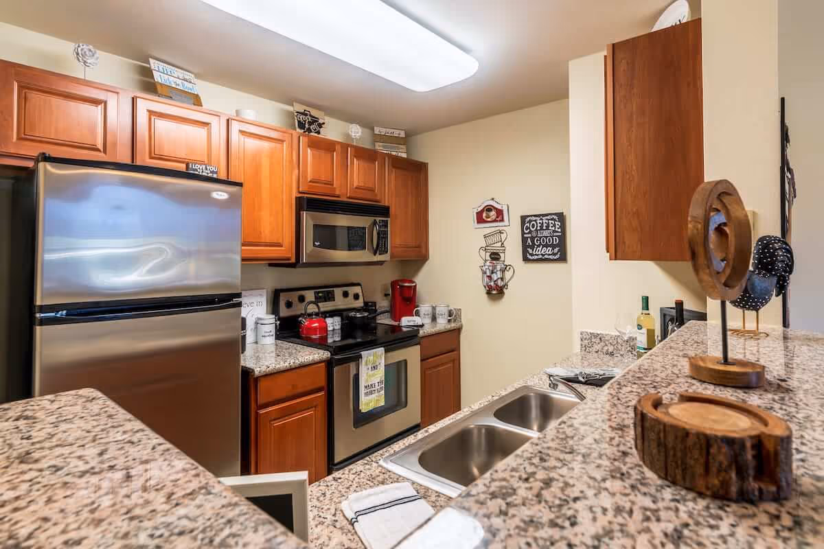Modern kitchen with stainless steel refrigerator and stove, wooden cabinets, granite countertops and a double sink.