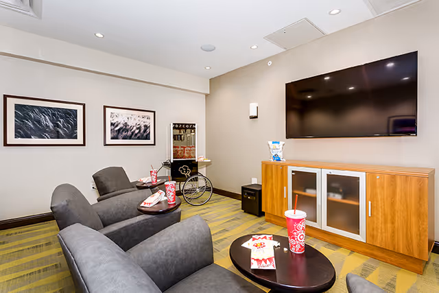 Small media room with three reclining chairs, a large wall-mounted TV, a popcorn cart, and snack cups on side tables.
