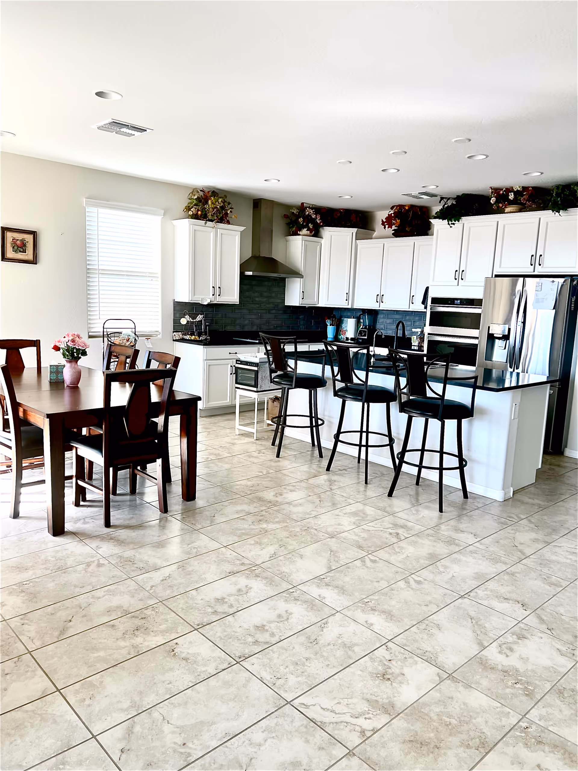 Bright open kitchen and dining area with white cabinets, a central island with bar stools, and a wooden dining table.