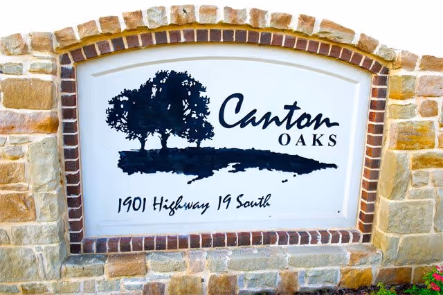 Stone and brick sign for Canton Oaks with a graphic of two oak trees and the address 1901 Highway 19 South.