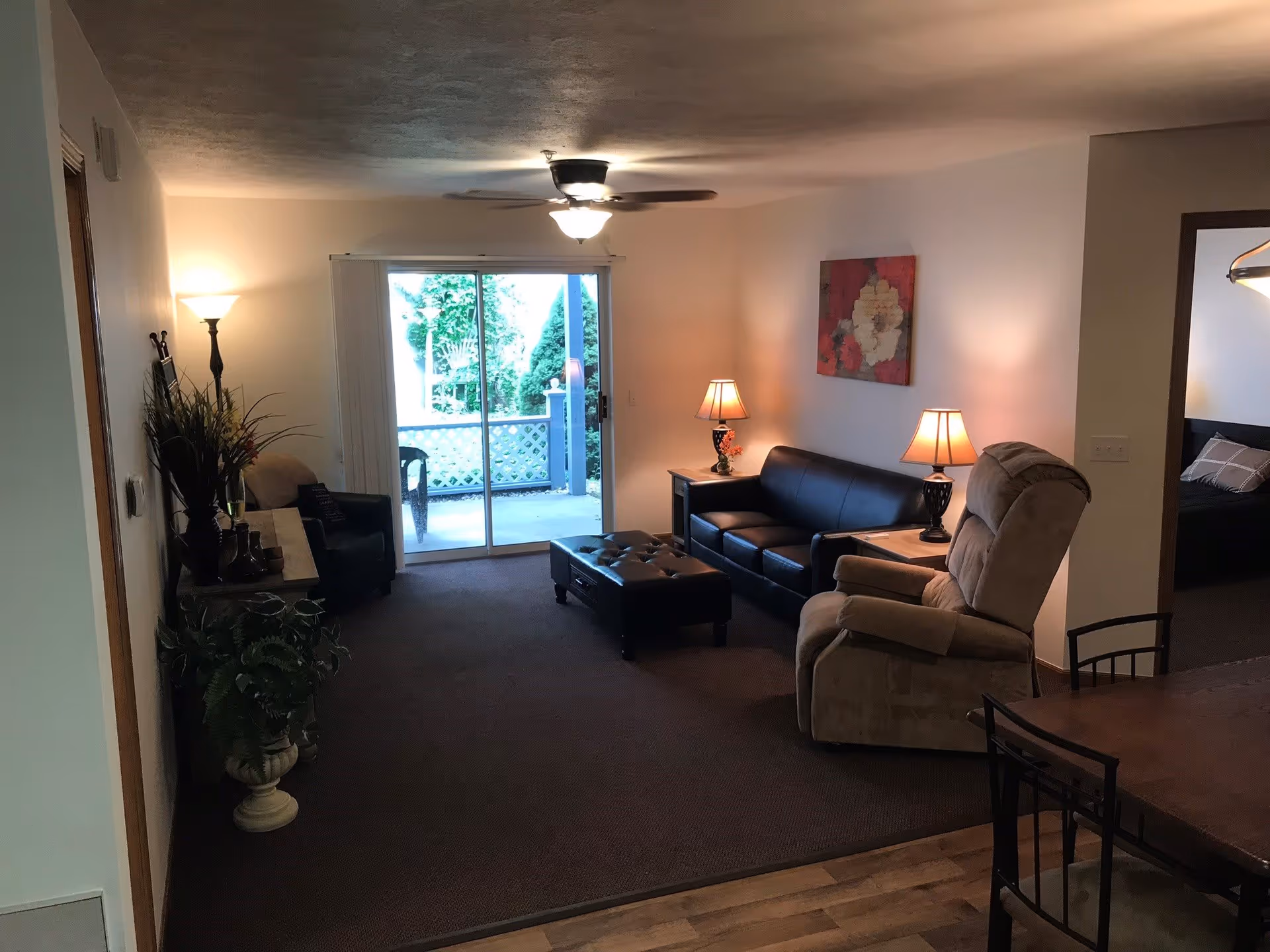 Living room with a sofa, recliner, ottoman and lamps facing a sliding glass door to an outdoor patio.