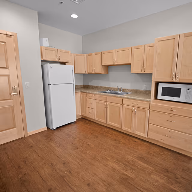 Small kitchen with light wood cabinets, laminate countertops, a sink, refrigerator, and microwave.