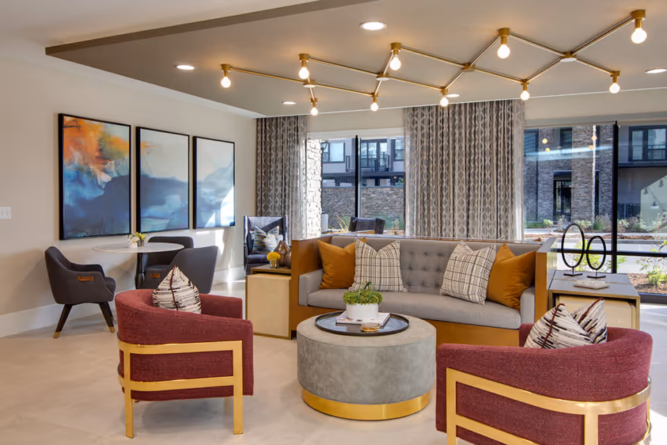 Bright, modern living room lounge with a sofa, accent chairs, round coffee table, dining nook, and large windows overlooking an outdoor courtyard.