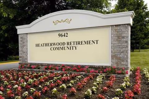 A large stone sign for Heatherwood Retirement Community sits beside colorful flower beds.