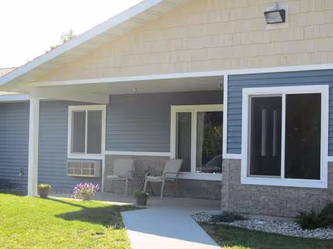 Front exterior of a blue-siding senior living facility with porch seating.