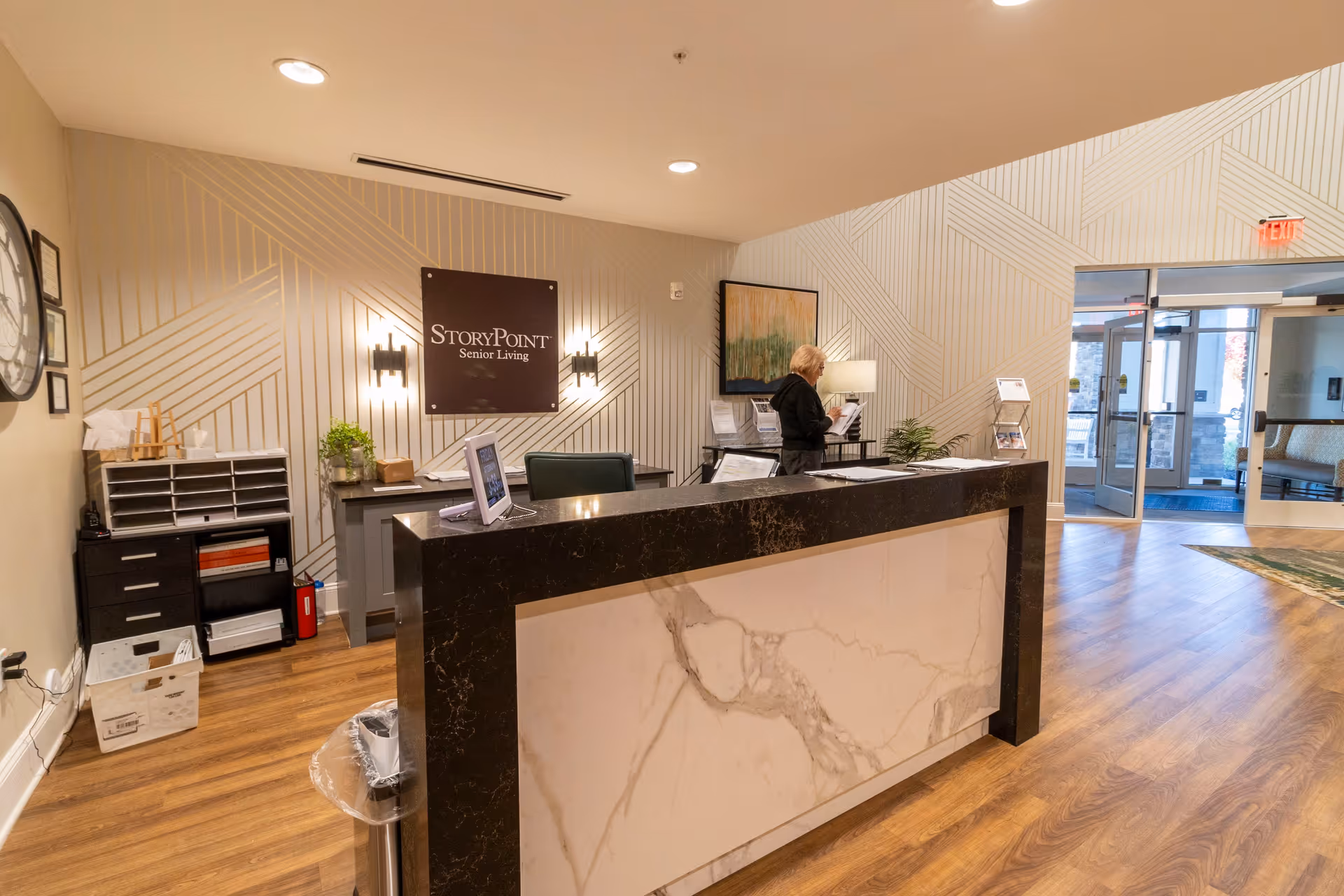 Reception desk and lobby area of StoryPoint Senior Living with a front desk, wall signage, and a staff member
