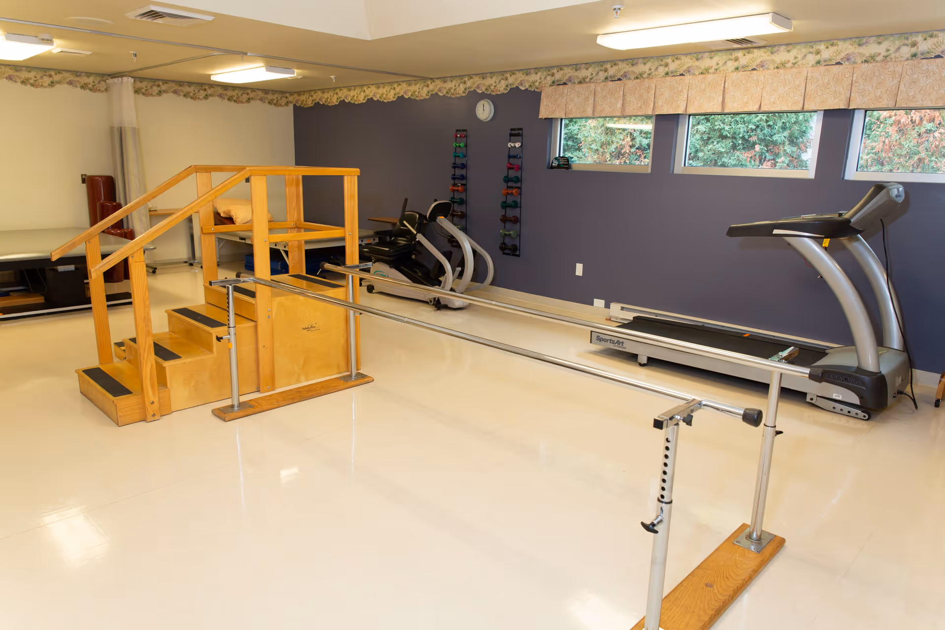 Rehabilitation exercise room with parallel bars, wooden practice stairs, treadmills, and a rack of dumbbells.