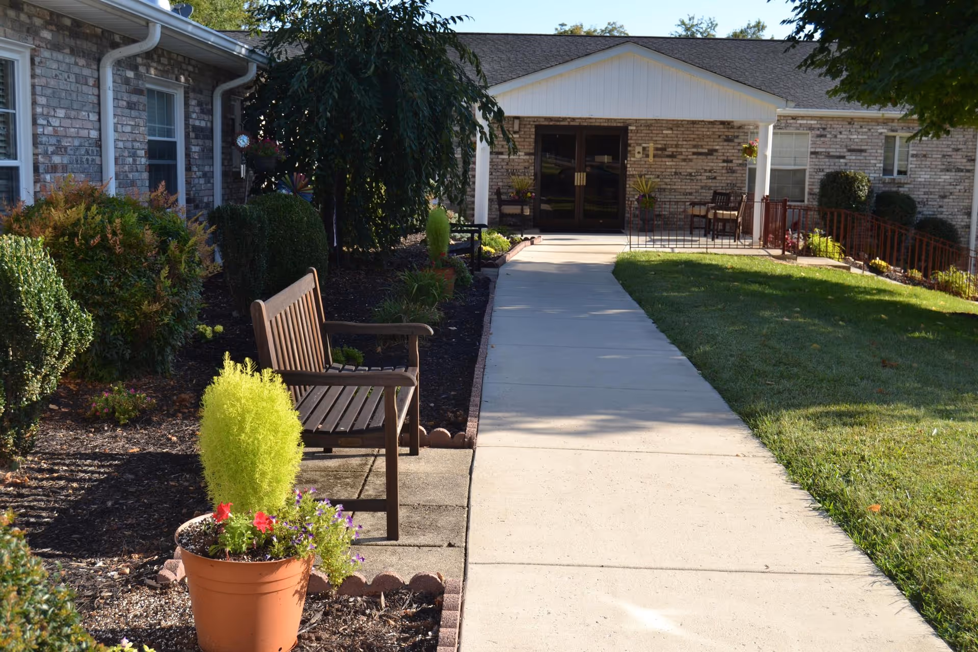 Walkway leading to the brick building entrance with benches, potted plants, and landscaped grounds.
