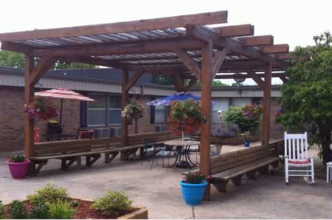 Wooden pergola-covered outdoor courtyard with benches, tables, and colorful potted plants.