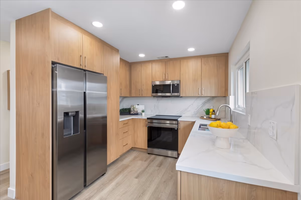 Modern kitchen with stainless steel refrigerator, oven and microwave, wood cabinets, and white marble countertops with a bowl of lemons.