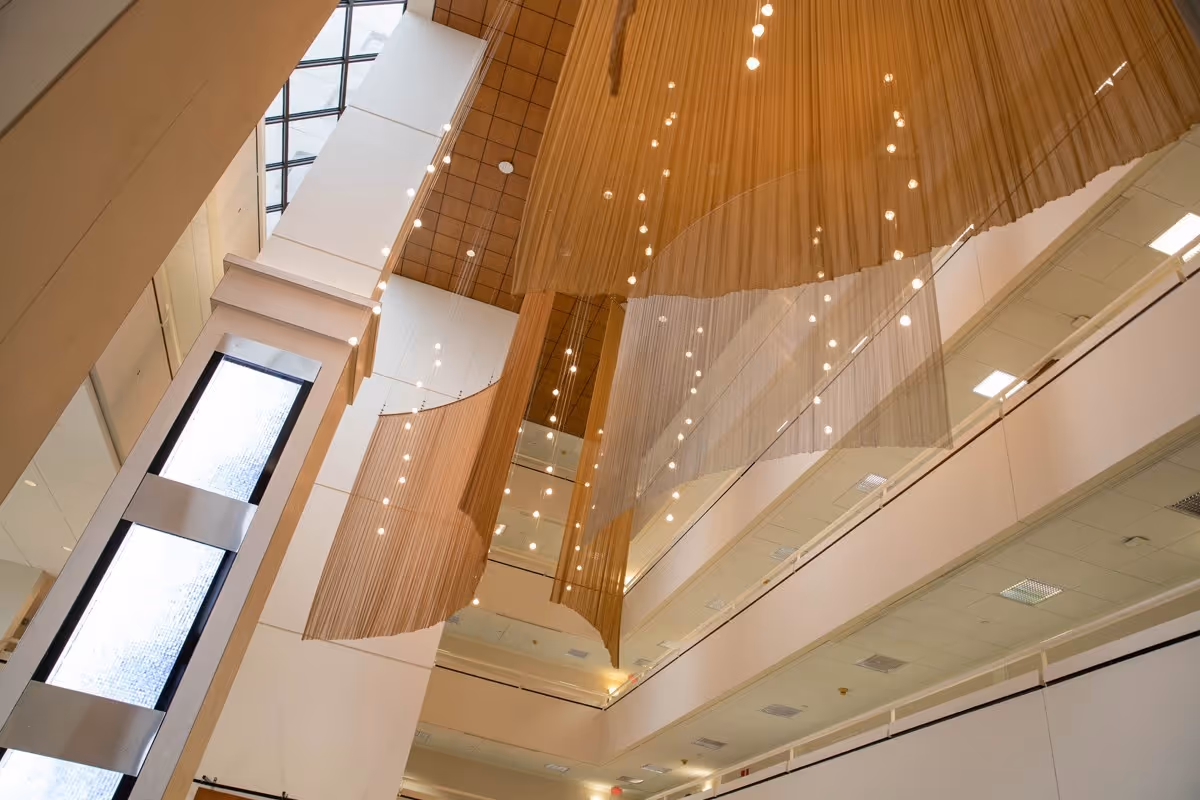 Interior view of a spacious, modern atrium with high ceilings, large windows, and hanging decorative light fixtures and curtains.