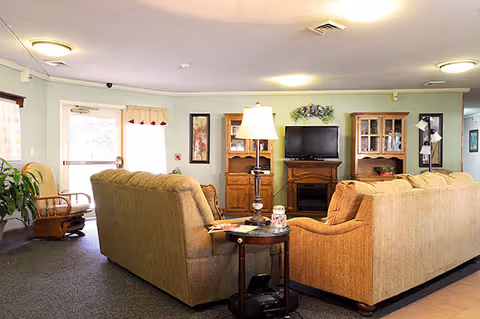 Cozy common room with two sofas facing a TV and cabinets, a side table with a lamp, and a doorway to the outside.