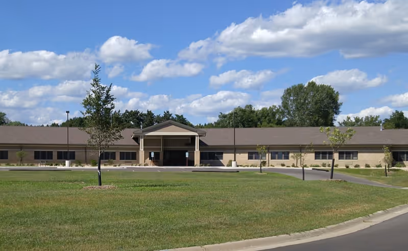 Long, single-story brick assisted living facility with a manicured lawn and entrance.