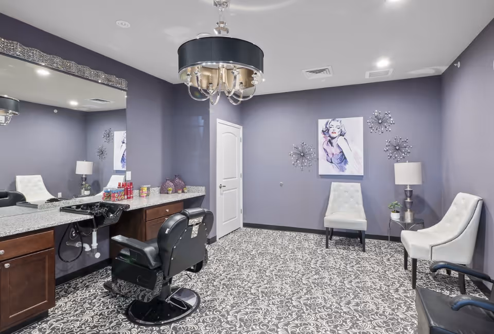 A stylish salon room with a barber chair at a granite counter and a small seating area against purple walls.