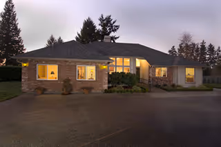 Single-story brick and siding senior care building at dusk with illuminated windows, a driveway, and trees in the background.