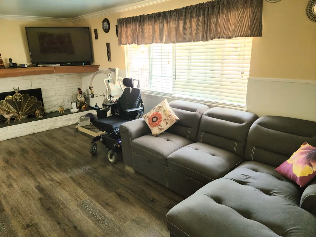 Bright living room with a sectional sofa, TV above a fireplace, and a motorized wheelchair near the window.