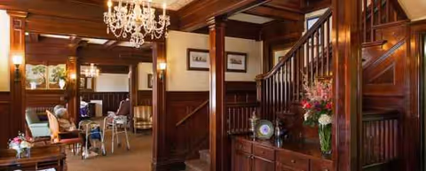 Wood-paneled living area with a chandelier, seating, staircase, and flowers.