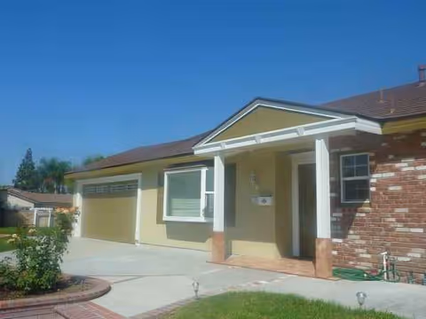 Single-story senior care facility with beige and brick exterior, front entrance, driveway, and lawn.