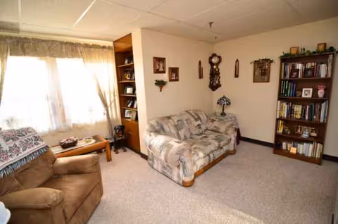 Cozy living room with beige sofas, bookshelf, clock, and large window.