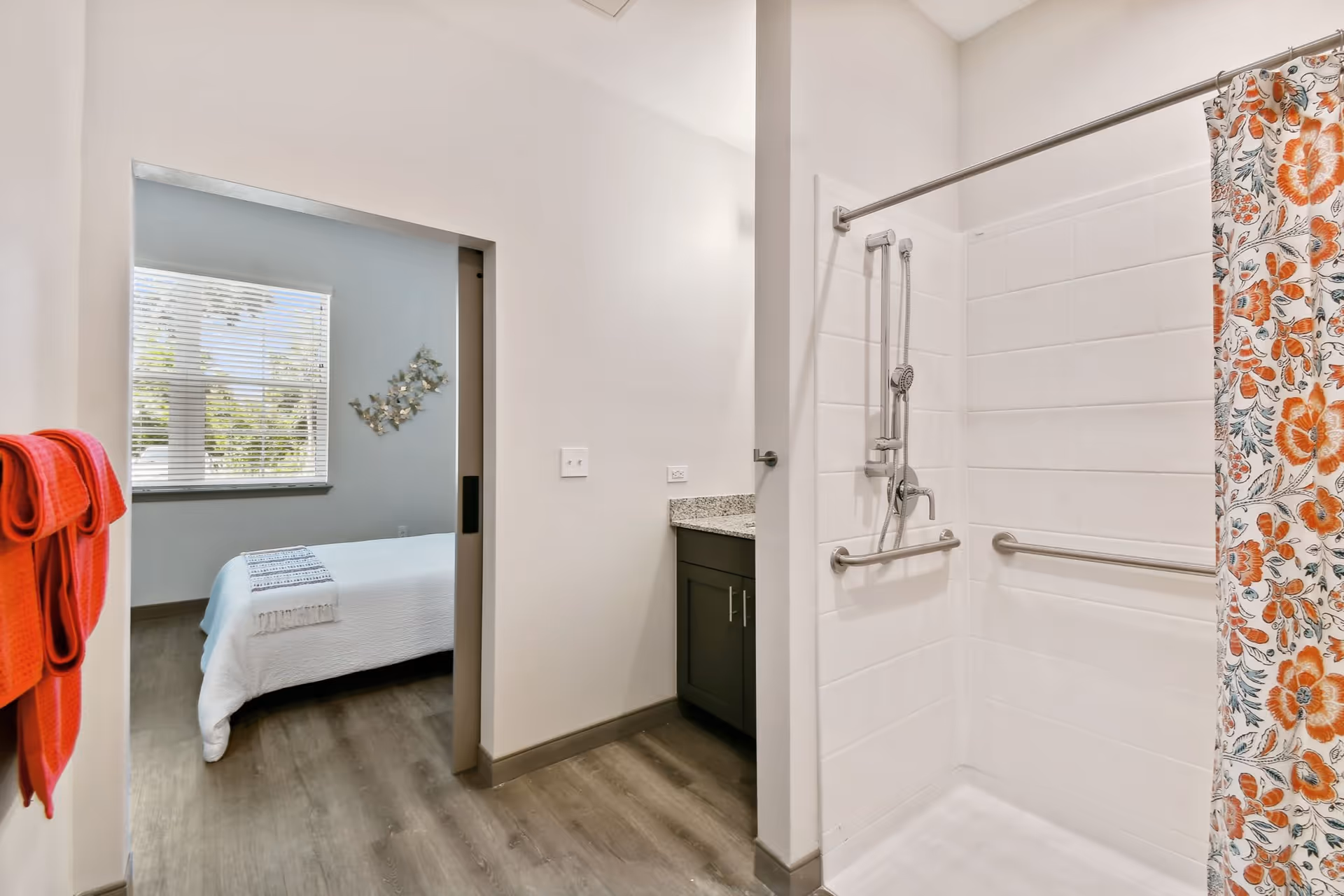 Accessible bathroom featuring a walk-in shower with grab bars and a floral shower curtain, opening into a bedroom.