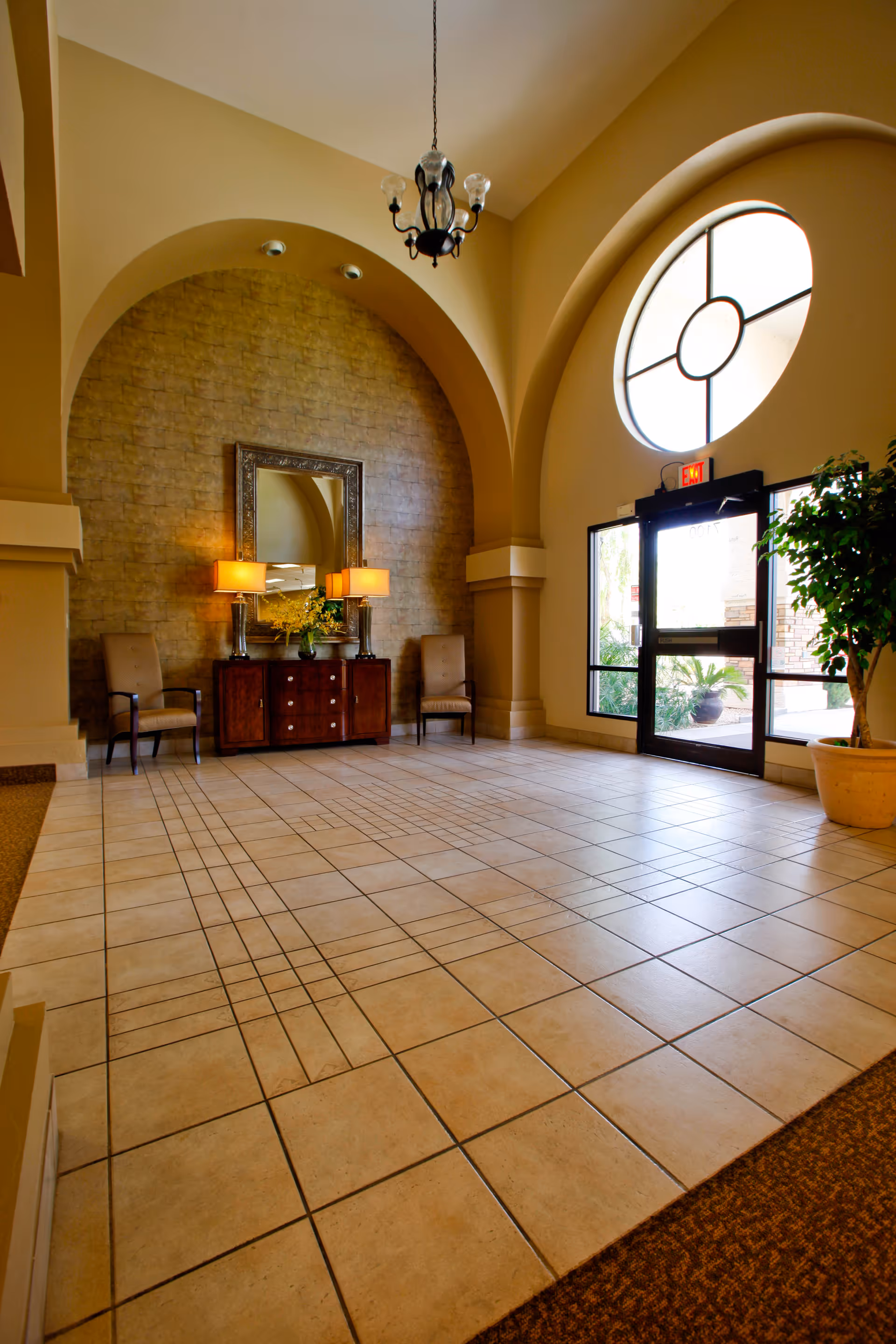 Spacious tiled lobby with arched ceilings, a decorative console table with lamps and seating, and a glass entrance door.