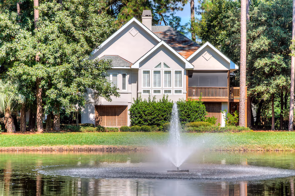 TidePointe building with large windows, wooden porch, and a fountain in front pond.