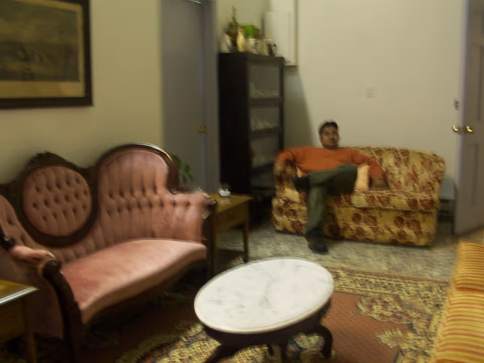 A person sits on a patterned sofa in a living room with vintage upholstered seating and a marble-top coffee table.