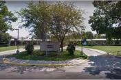 Exterior view of Avera Mother Joseph Manor Retirement Community showing a circular driveway with a landscaped island in the center featuring trees and a sign with the facility's name. The building is single-story with a flat roof and surrounded by green lawns and additional trees.