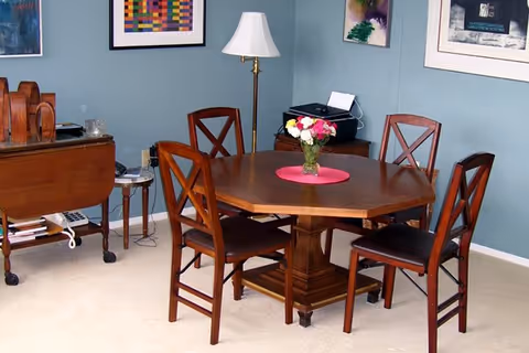 Wooden dining table with four chairs and a vase of flowers in a cozy room with teal walls and framed art.