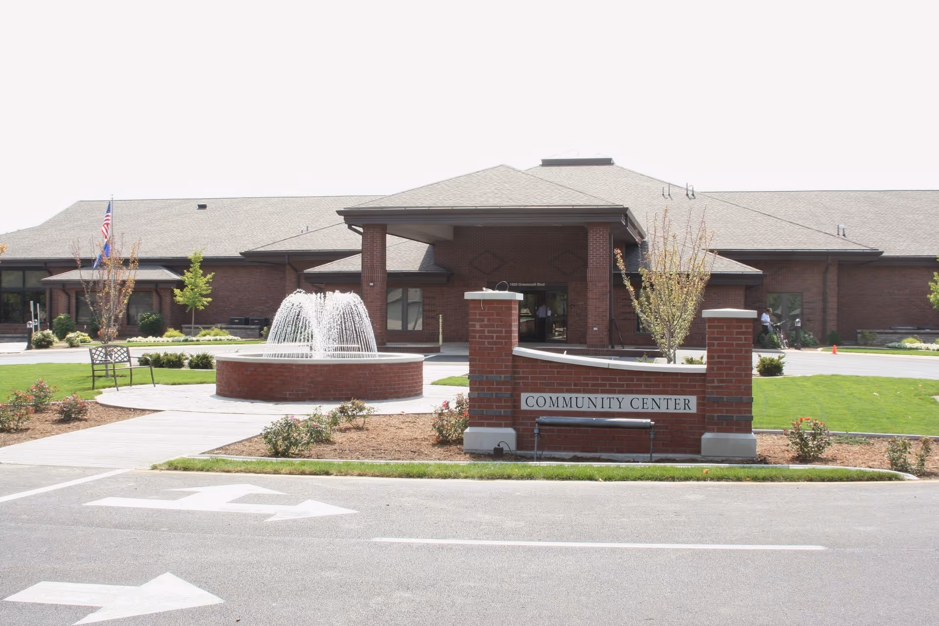 Front of a brick community center building with a circular fountain and a 'COMMUNITY CENTER' sign in the foreground.