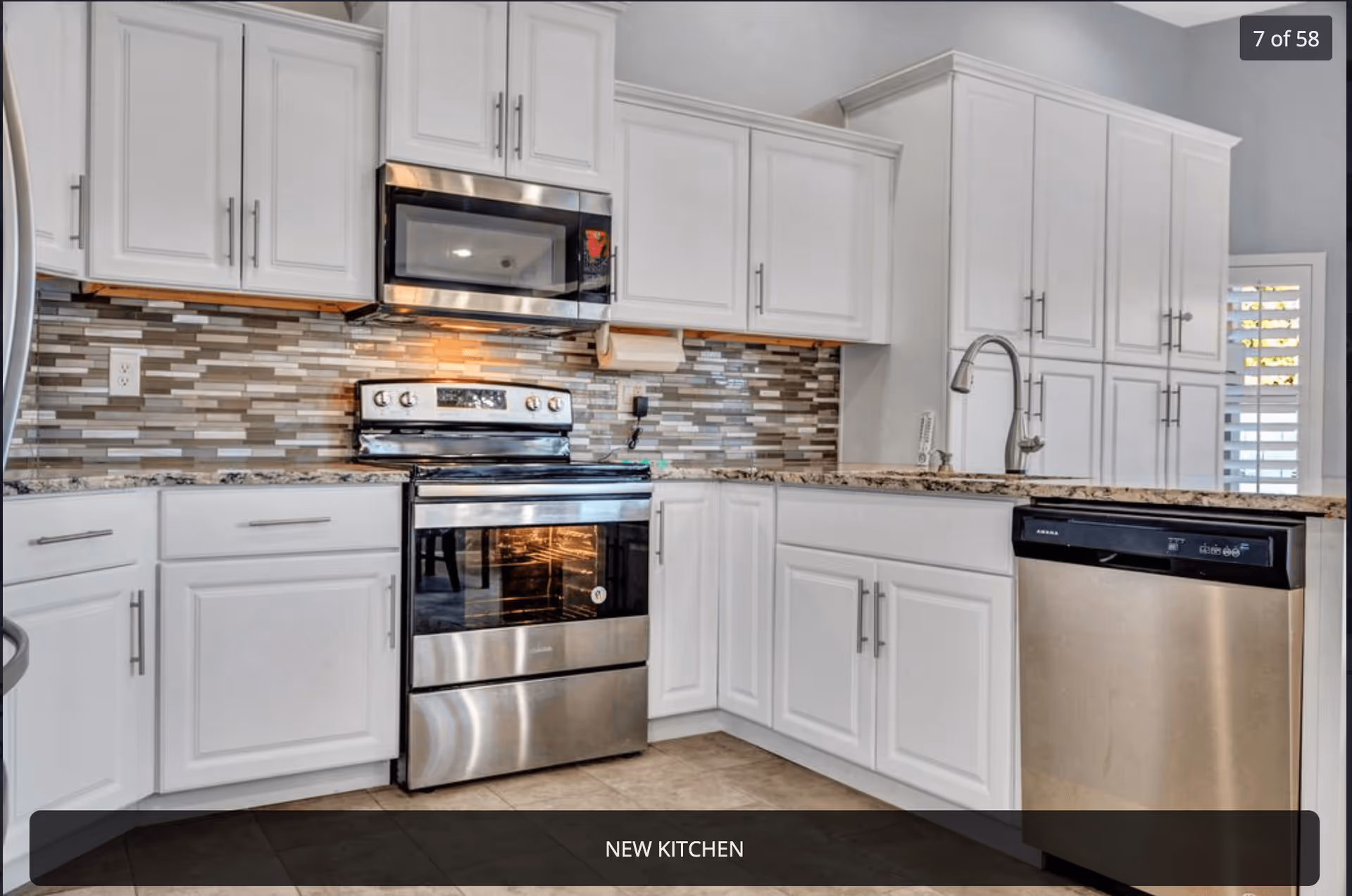 Modern kitchen with white cabinets, stainless steel appliances including a stove, microwave, and dishwasher, granite countertops, and a tiled backsplash.